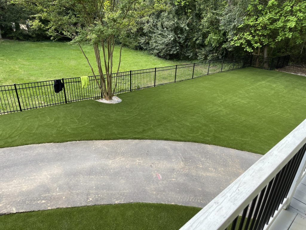 Backyard artificial grass lawn with black fence